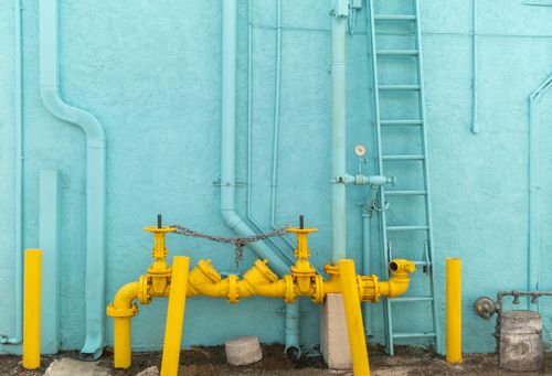 Image is of yellow pipes against teal building concept of Southwest Ranches plumbing services