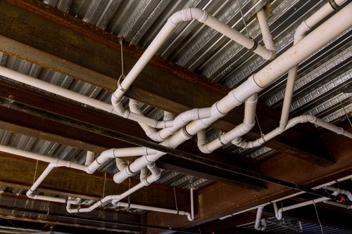 Image is of plumbing pipes running along a ceiling in an industrial building concept of Palm Beach commercial plumbing